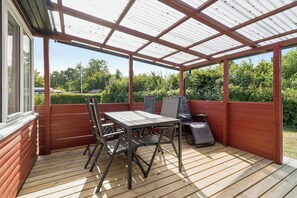 A covered patio with a table and chairs, a grill, and a view of the surrounding greenery. - Lovely holiday home by Fjellerup Beach (Glesborg)