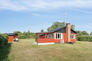 A red wooden house with a chimney, a small porch, and a lawn. - Lovely holiday home by Fjellerup Beach (Glesborg)
