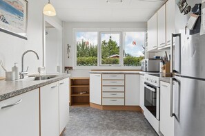 Eine moderne Küche mit weißen Schränken, einem Edelstahlkühlschrank und einem Fenster mit Blick auf Bäume und Himmel.
