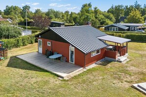 Ein eingeschossiges Haus mit geneigtem Dach, einer überdachten Terrasse und einer kleinen Holzterrasse.