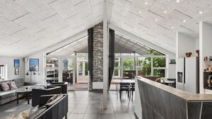 A spacious living area with a high ceiling, a fireplace, and a view of the outdoors. - Large holiday home with spa and games room (Brovst)