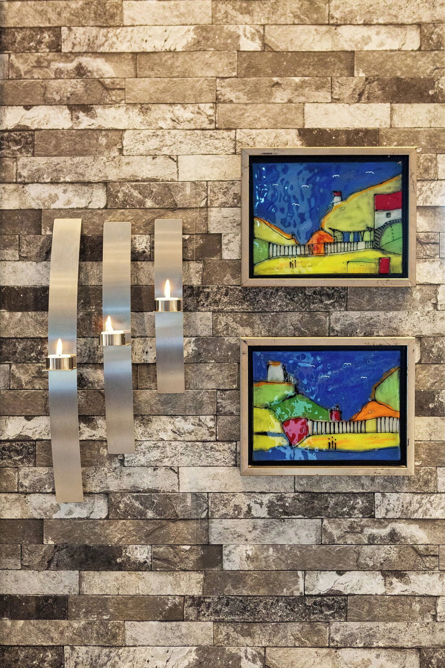 A wall with a textured stone pattern and two framed paintings.