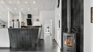 A modern kitchen with a central island, a stove with a glass door, and a hallway leading to another room. - Large holiday home with spa and games room (Brovst)