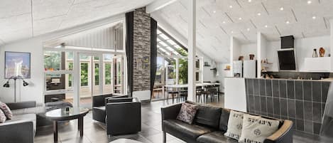 Um interior moderno com área de estar, lareira e vista através de grandes portas de vidro.