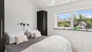 A bedroom with a bed, bedside lamps, a window with a view of greenery and a house, and a white ceiling. - Large holiday home with spa and games room (Brovst)
