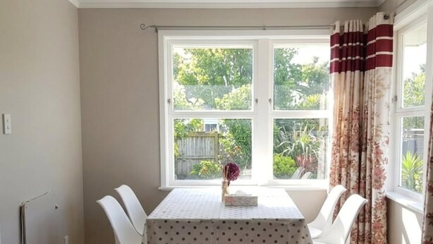 A dining area with a table set for four, a window with curtains, and a view of greenery outside.