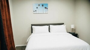 A hotel room with a bed, a nightstand, a lamp, and a painting of palm trees on the wall.