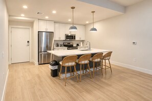 A modern kitchen with stainless steel appliances, a central island with bar stools, and pendant lighting. - Spacious Luxury North Retreat with Pool and Gym (Naples)