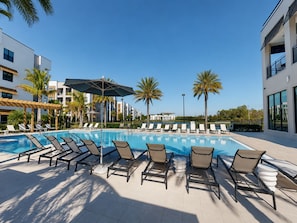 A pool area with lounge chairs and umbrellas, surrounded by palm trees and modern buildings. - Spacious Luxury North Retreat with Pool and Gym (Naples)