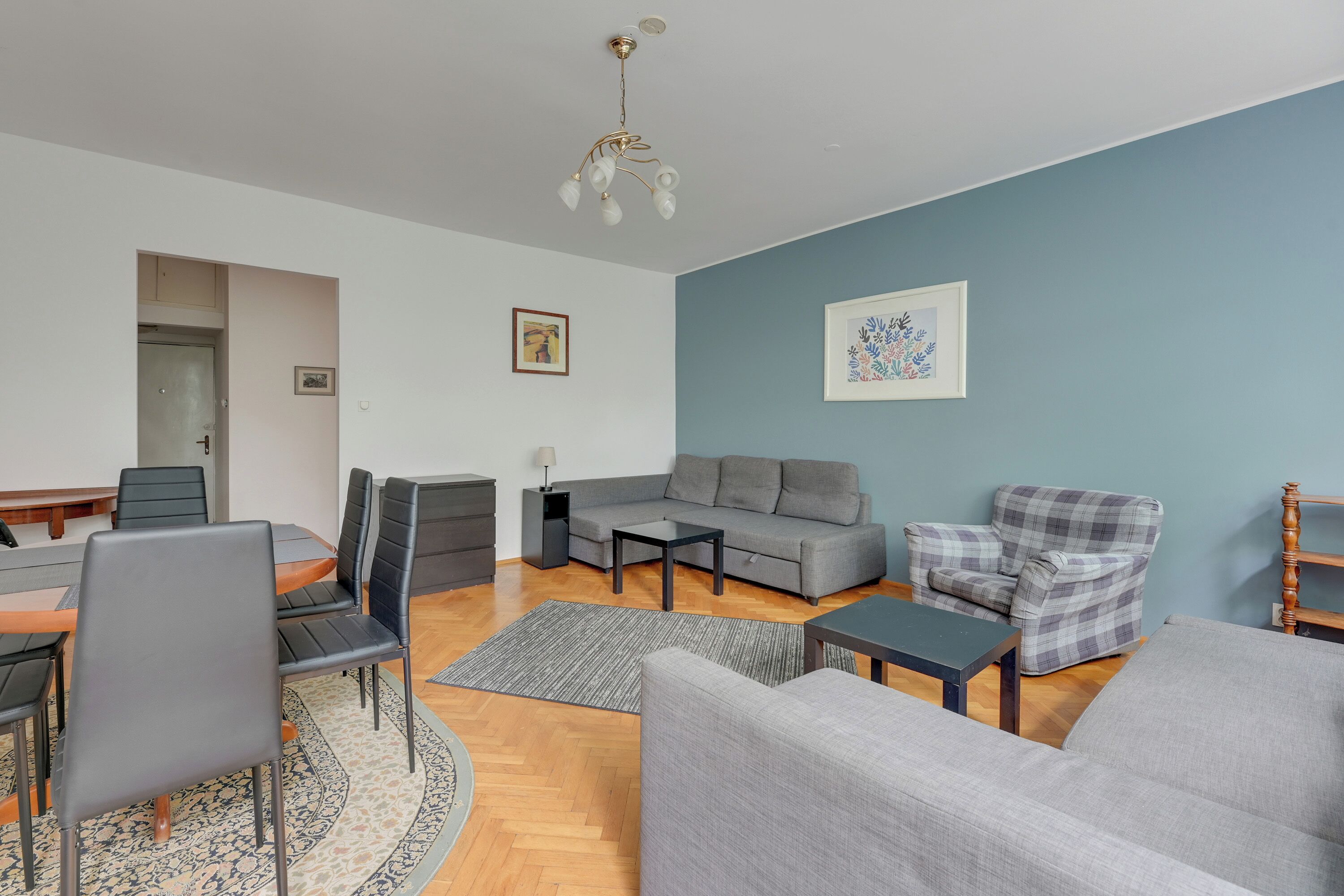A modern living room with a grey sofa, a plaid armchair, a dining table with chairs, and a small side table.