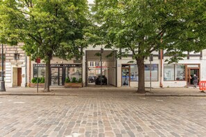 Une rue pavée bordée d’arbres, avec des devantures de magasins et un passage piéton.