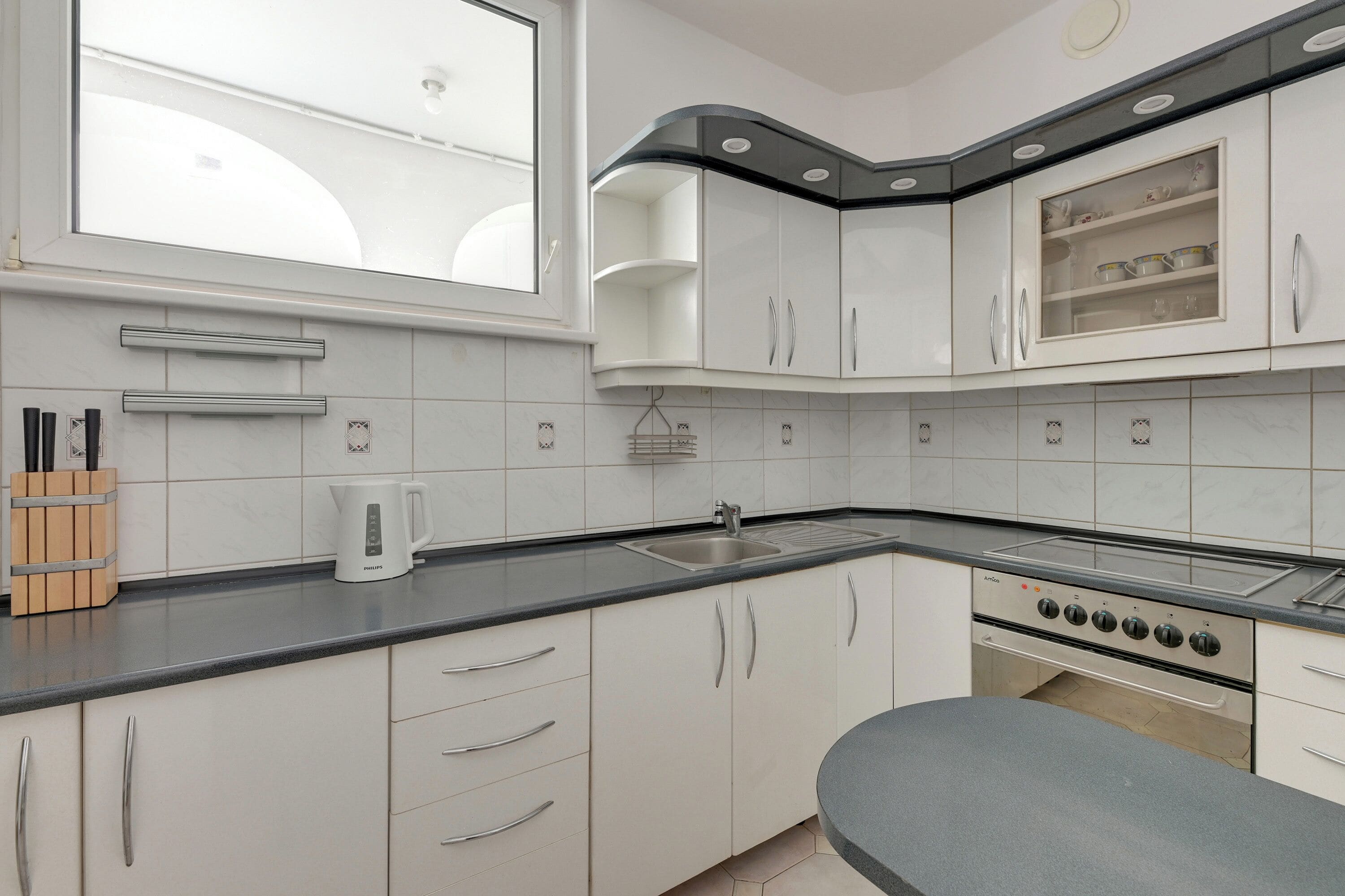 A modern kitchen with white cabinets, a black countertop, a built-in oven, and a window above the sink.