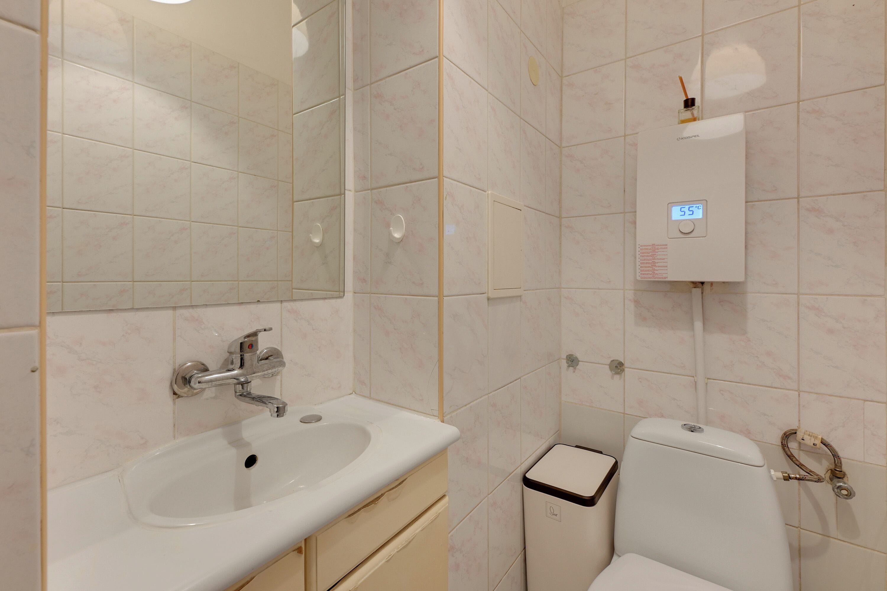 A bathroom with a sink, mirror, toilet, and a wall-mounted heater.