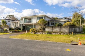 A two-story house with a garage, a front yard with a fence, and a street with a traffic cone. - Family Haven, Lake Taupō Escape (Taupō)