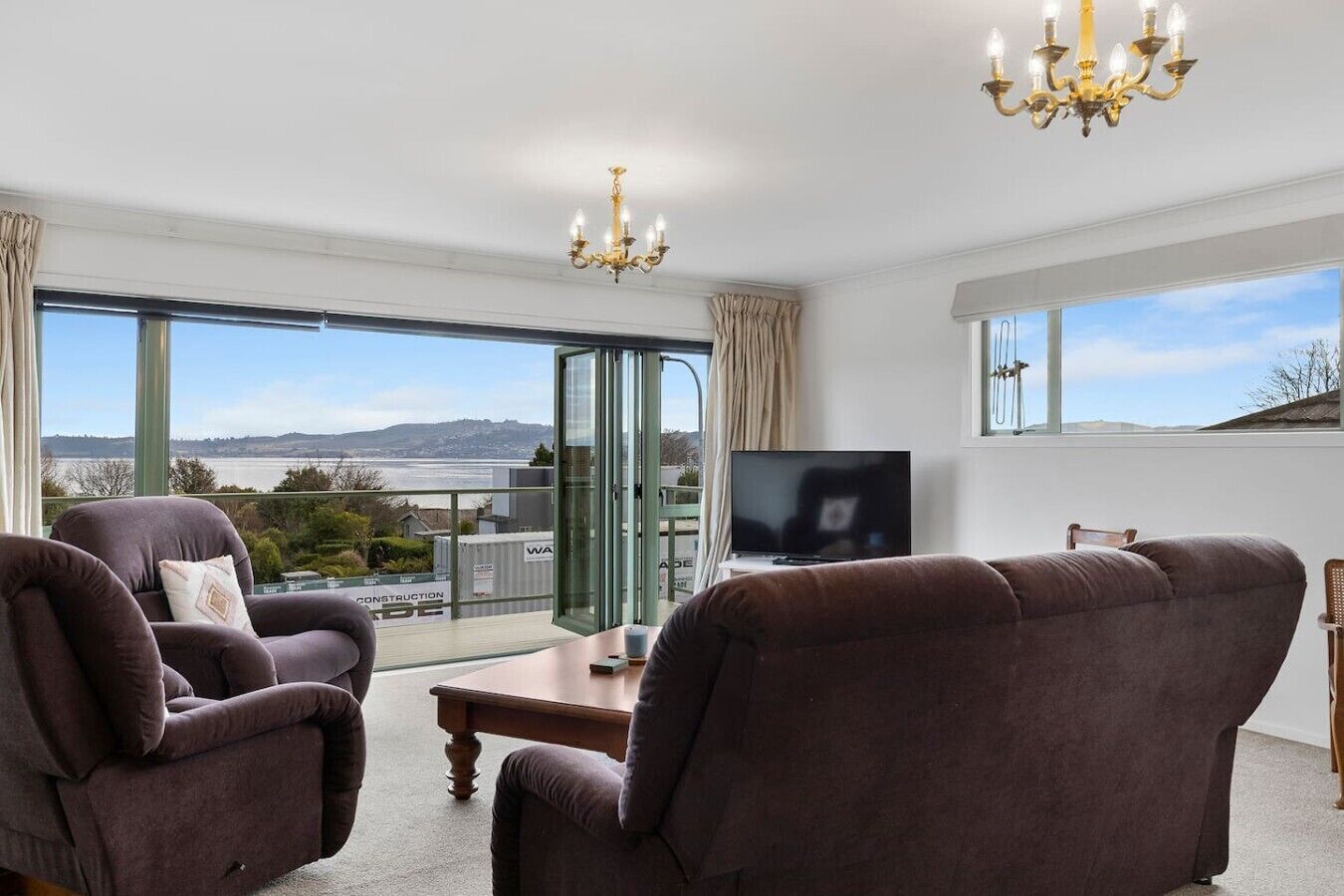 A modern living room with a television, two armchairs, a coffee table, and a view of the city through large windows.