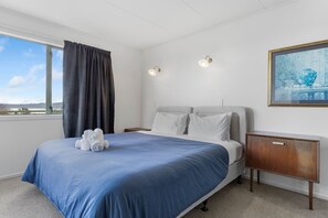 A hotel room with a bed, a nightstand, a painting, and a window with curtains. - Family Haven, Lake Taupō Escape (Taupō)