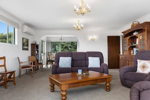 A living room with a sofa, armchairs, a coffee table, a chandelier, and a wooden cabinet. - Family Haven, Lake Taupō Escape (Taupō)