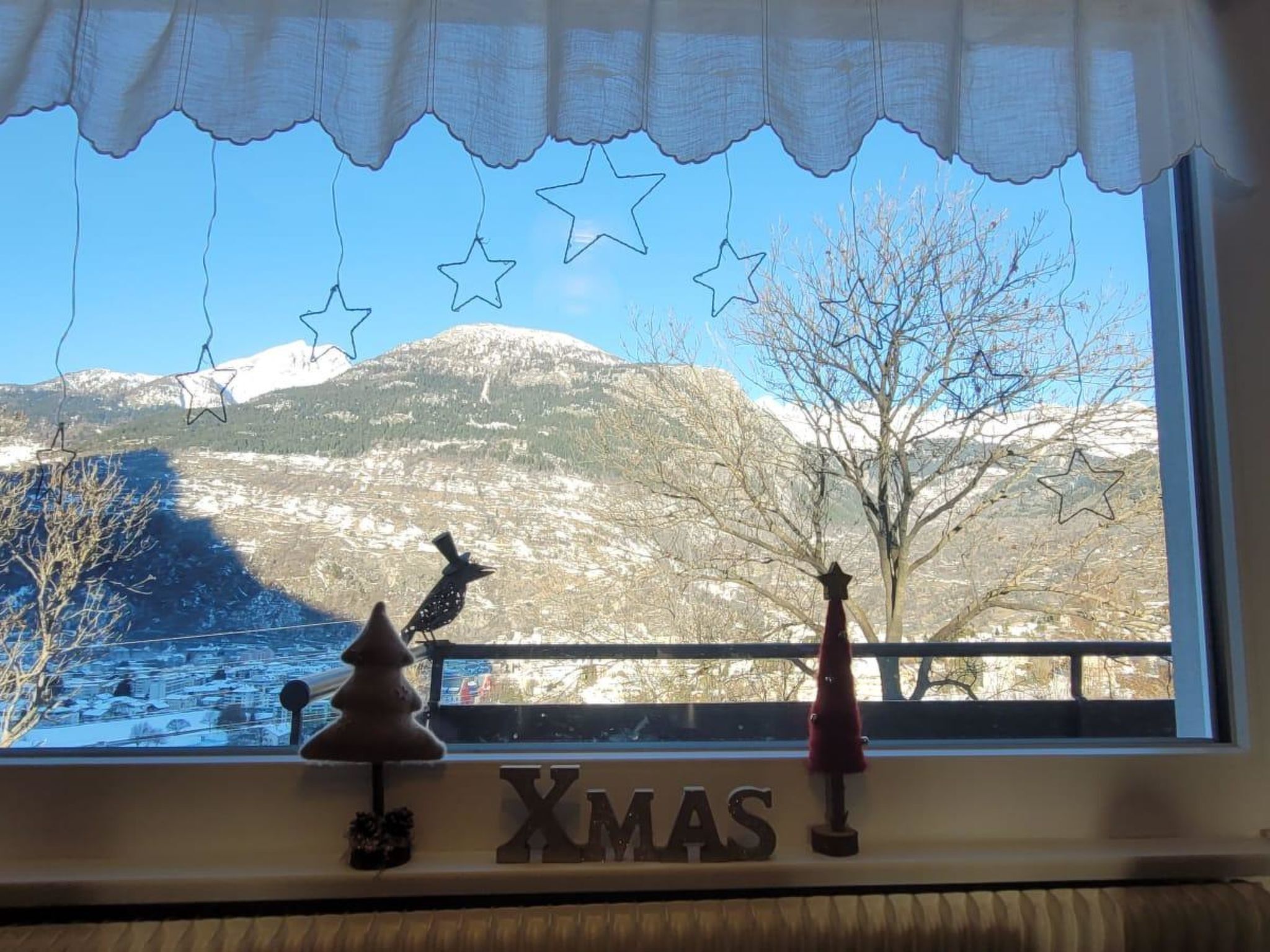 Une fenêtre donnant sur un paysage enneigé, un sapin de Noël et une figurine d’oiseau.