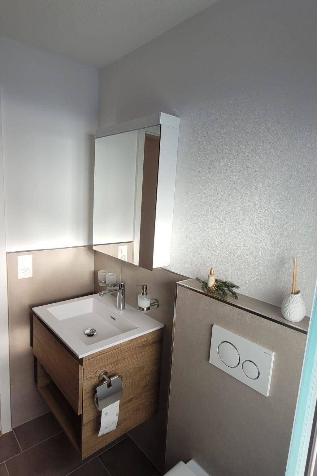 Uma casa de banho moderna com toucador de madeira, um espelho grande e um candeeiro fixo na parede.