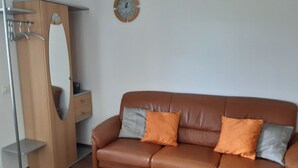Ein braunes Ledersofa mit zwei Kissen, ein Holzschrank und eine Wanduhr.