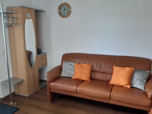 Ein braunes Ledersofa mit zwei Kissen, ein Holzschrank und eine Wanduhr.