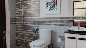 Et badeværelse med bruser, toilet, vask og en dekorativ vægdekoration.