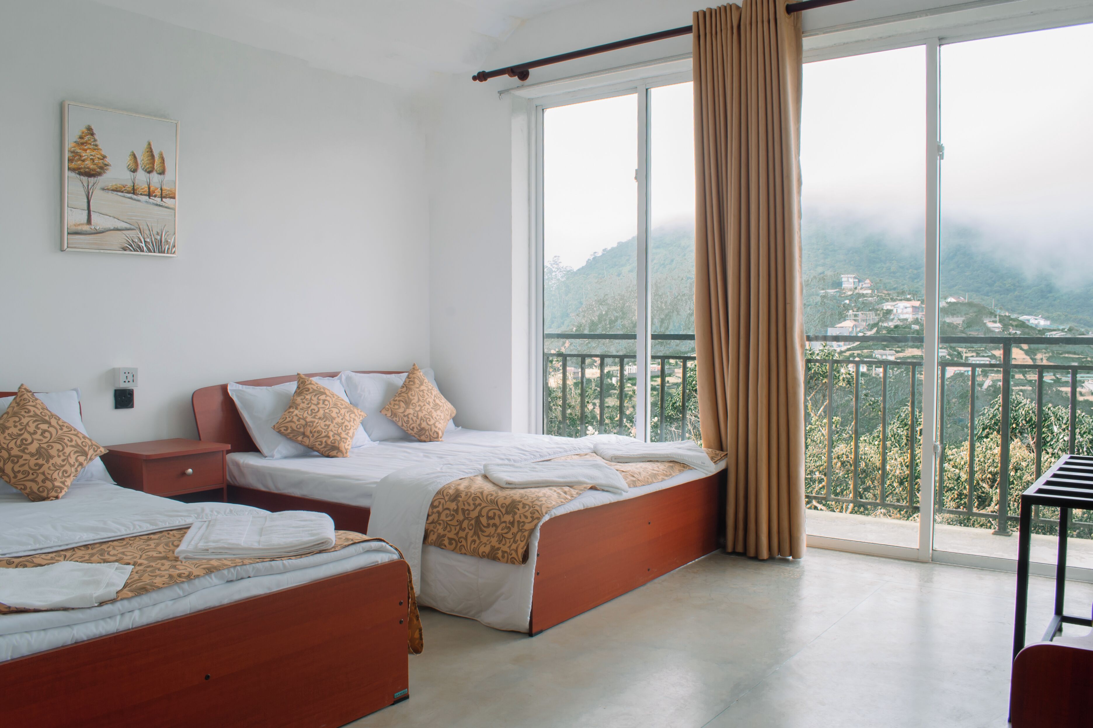 Ein Hotelzimmer mit zwei Betten, einem Bild an der Wand und einem Balkon mit Bergblick.