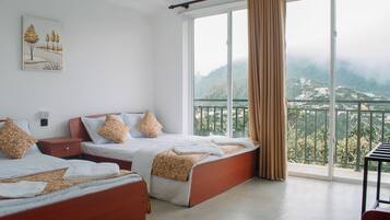Ein Hotelzimmer mit zwei Betten, einem Bild an der Wand und einem Balkon mit Bergblick.