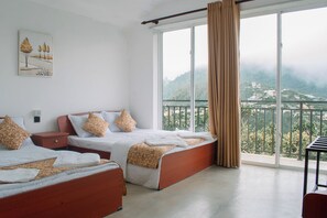 Quarto de hotel com duas camas, um quadro na parede e uma varanda com vista para as montanhas.