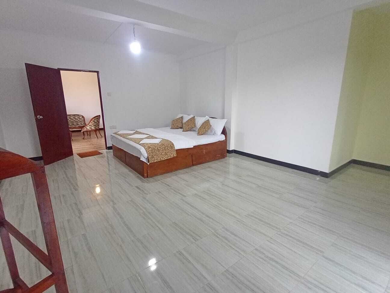 A spacious room with a bed, a wooden chair, and a door leading to another room.