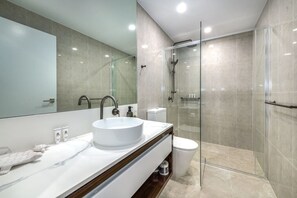 Un baño moderno con un espejo grande, un lavabo redondo, inodoro y zona de ducha con mampara de cristal.