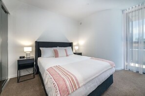 Ein Hotelzimmer mit einem großen Bett, zwei Nachttischen mit Lampen, einem Fenster mit leichtem Vorhang und einem Teppichboden.