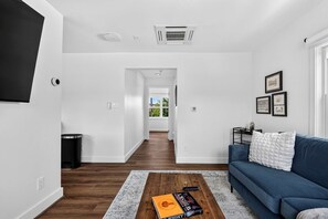 Ein modernes Wohnzimmer mit einem blauen Sofa, einem Couchtisch mit einem Buch und einem Flur, der in ein weiteres Zimmer führt.