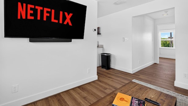 A modern living room with a large flat-screen TV mounted on the wall displaying the word 'NETFLIX' in red letters. - Iconic urban Bourbon Trail suite with EV charger! (Louisville)