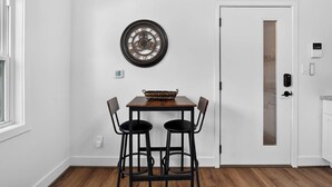 A dining area with a wooden table, two chairs, and a wall-mounted clock. - Iconic urban Bourbon Trail suite with EV charger! (Louisville)