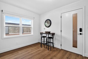 Een kamer met een houten vloer, een witte deur en een raam met uitzicht op een bakstenen muur.