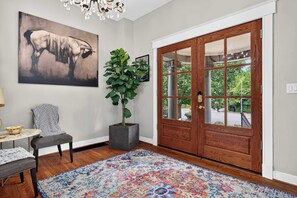 A room with a large wooden door, a potted plant, a colorful rug, a framed artwork, and a small table with a bowl. - 4-Bedroom Louisville Apartment | Backyard, Office (Louisville)
