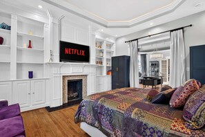 Ein Schlafzimmer mit einem großen Bett, einem Kamin, einem darüber montierten Fernseher und einem Bücherregal.