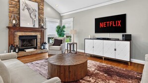 Un salon avec une cheminée en pierre, une table basse ronde, un canapé, un téléviseur fixé au mur et un meuble sur lequel on peut voir le logo de Netflix.