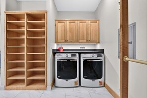 A laundry room with two washing machines, a wooden shelving unit, and a cabinet. - 4-Bedroom Louisville Apartment | Backyard, Office (Louisville)