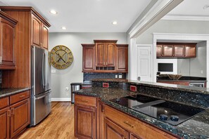Eine Küche mit Holzausstattung, einem Edelstahl-Kühlschrank, einer Granit-Arbeitsplatte und einer Wanduhr.