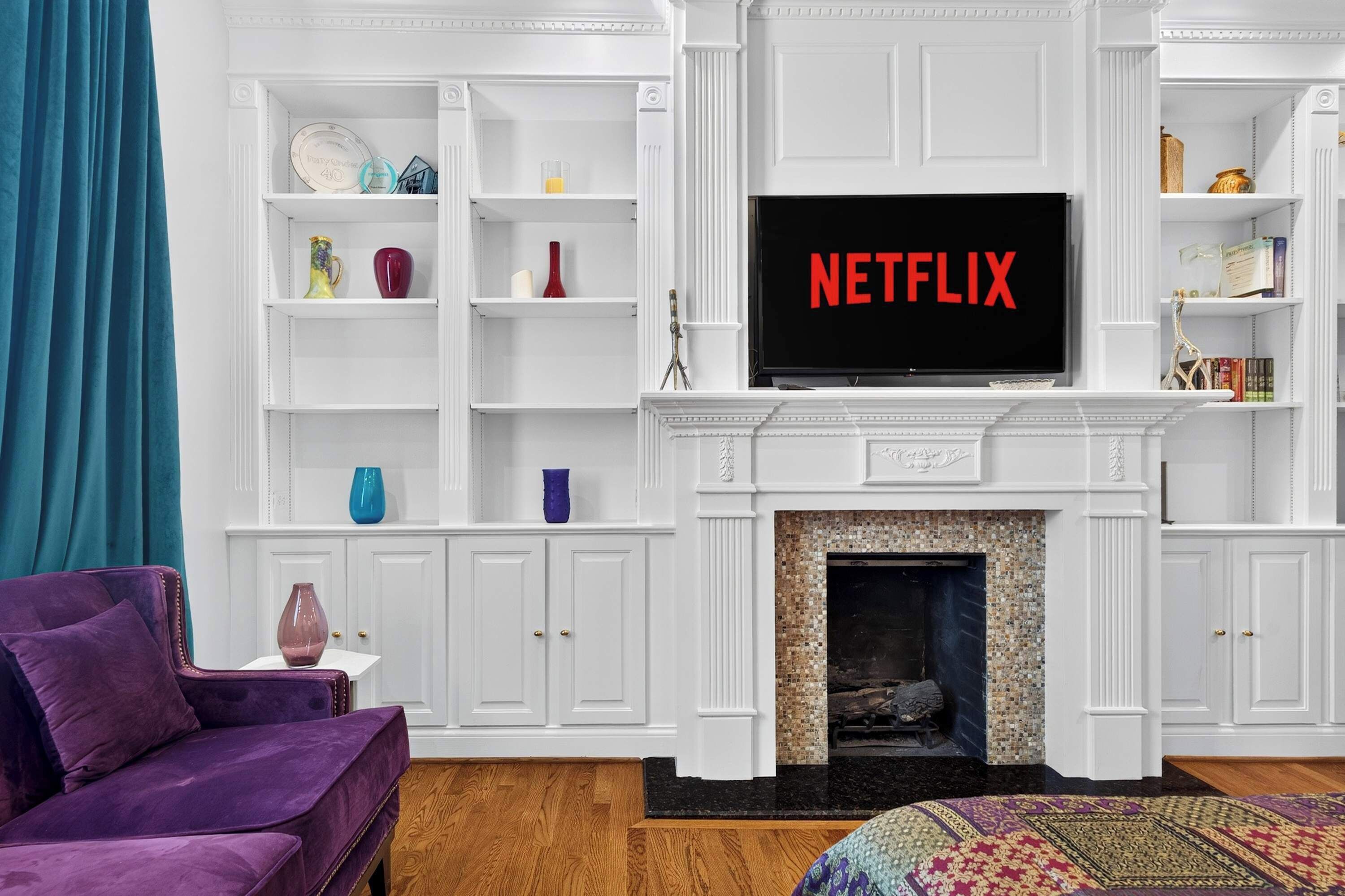 A living room with a fireplace, a television displaying 'NETFLIX', and a purple armchair.
