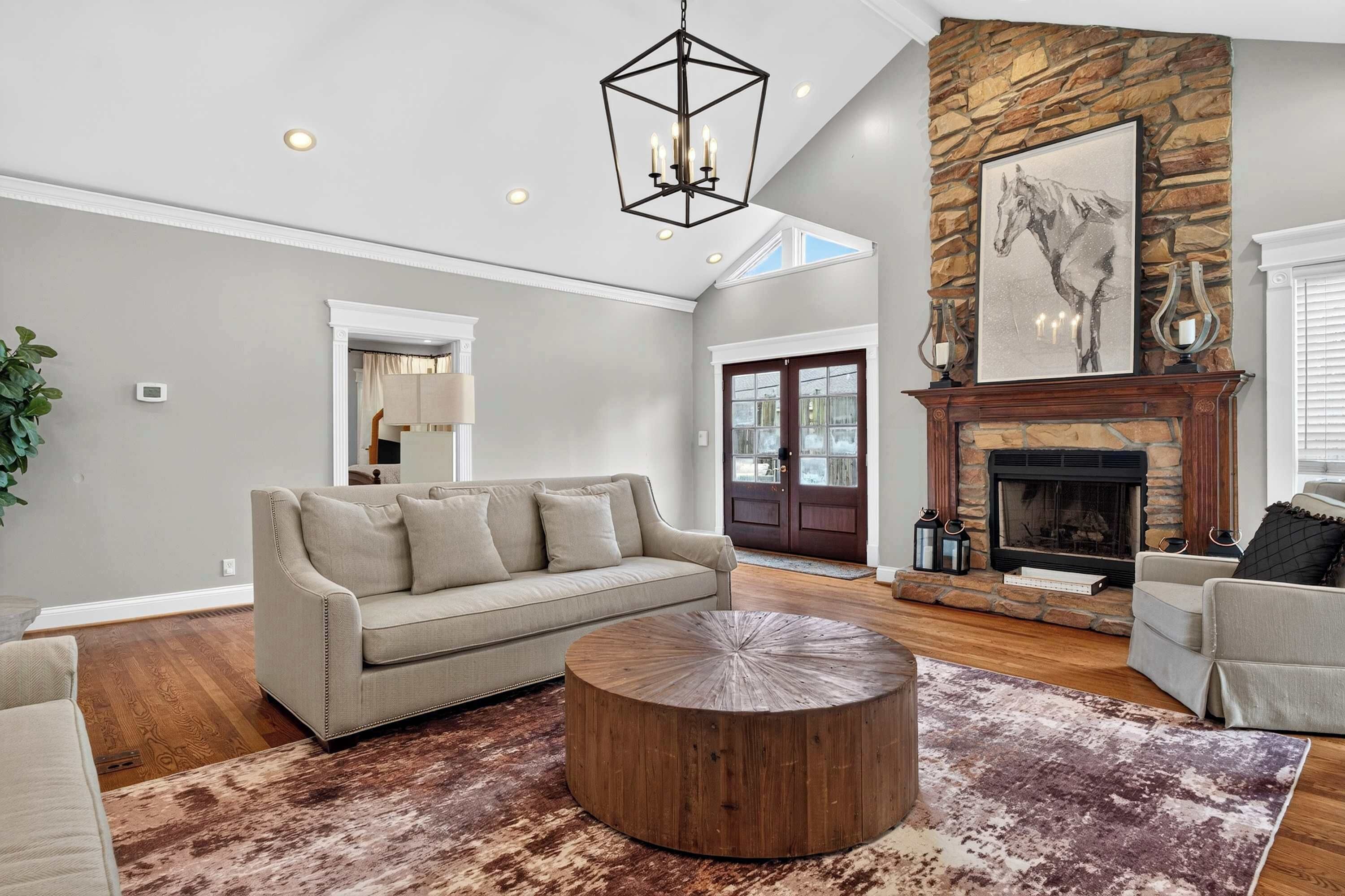 A spacious living room with a stone fireplace, a large painting, and a modern chandelier.