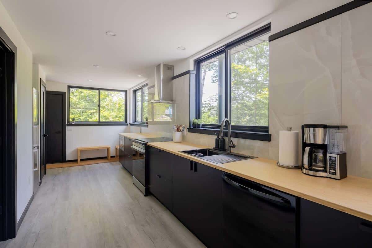 A modern kitchen with black cabinets, a wooden countertop, a sink, and a coffee maker.