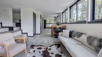 Una sala de estar moderna con un sofá, una mesa de centro y un tapete de cuero de vaca. Se ve una escalera que sube a otro nivel.