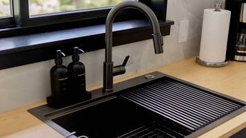 Una cocina moderna con un lavamanos negro, encimera de madera y ventana con vista a árboles.