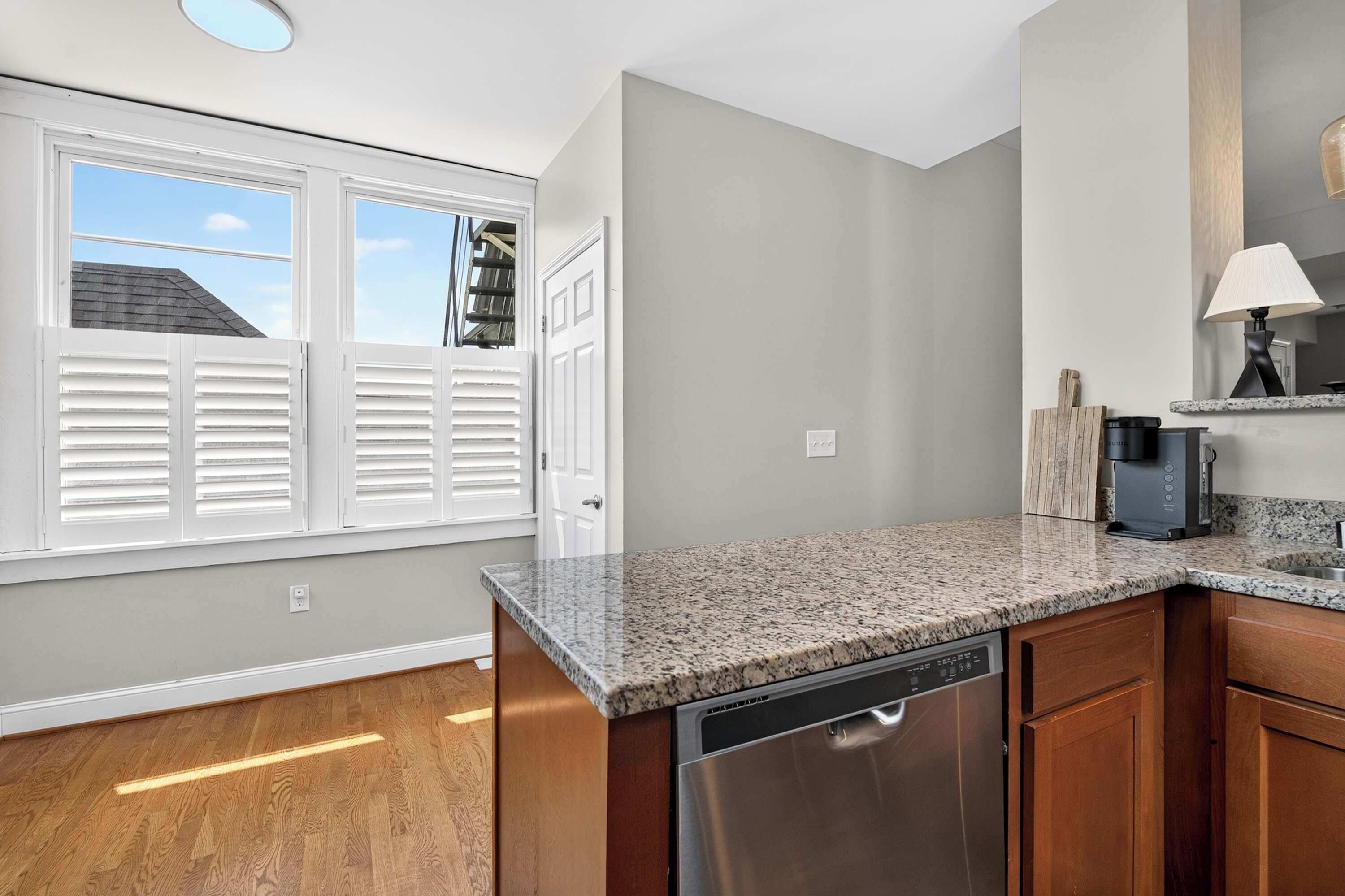 A kitchen with a dishwasher, a coffee maker, and a window with blinds.