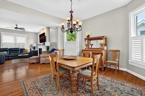 Un salón amplio con un sofá de cuero oscuro, una mesa de comedor de madera con sillas y una araña.
