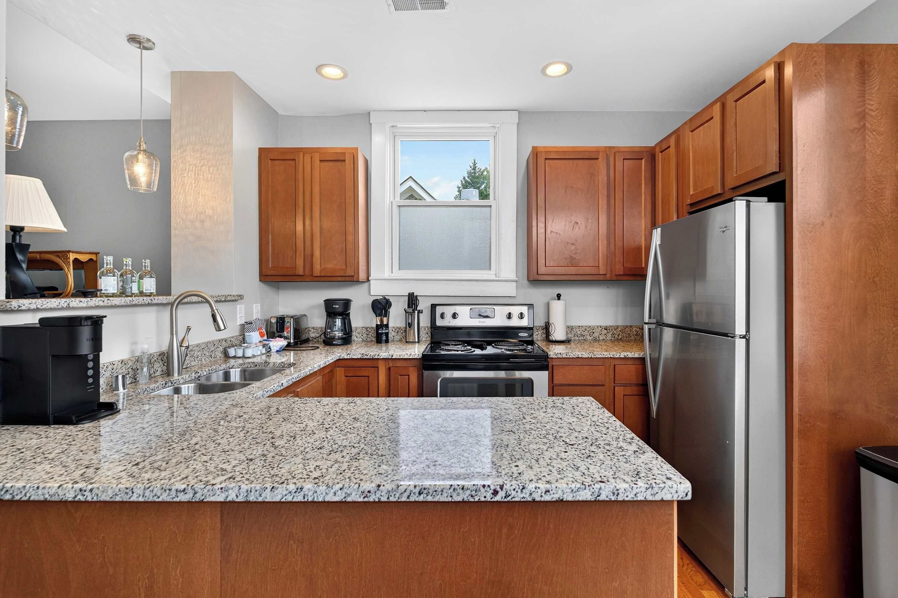 A modern kitchen with granite countertops, stainless steel appliances, wooden cabinets, and a window with a view of the outside.