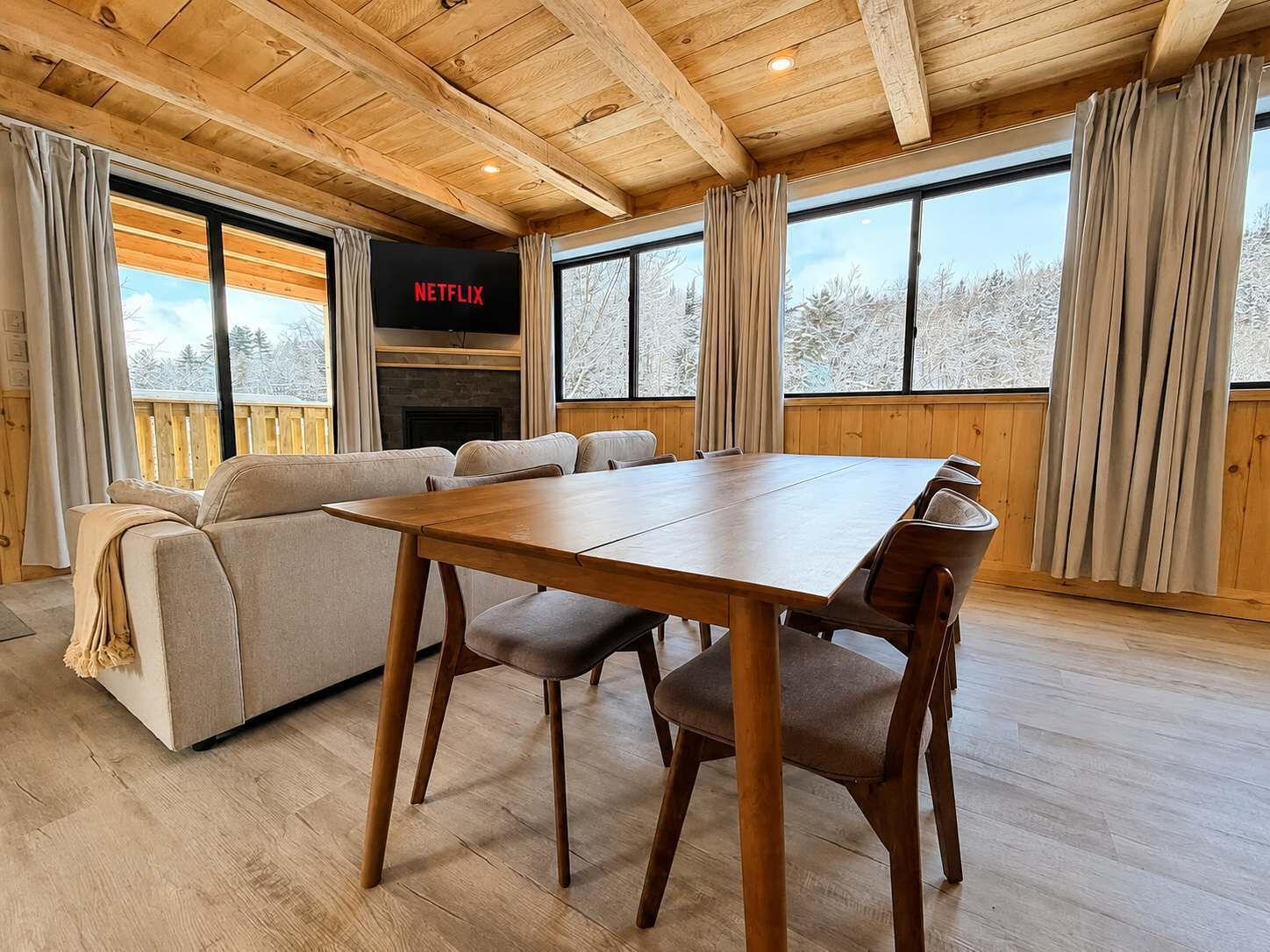 A cozy room with a wooden ceiling, a sofa, a dining table, and a fireplace.